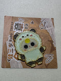 Baby Three Panda enamel pin with black ears and paws and yellow forehead detail on backing card