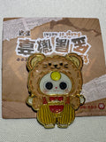Baby Three Secret enamel pin with brown animal hood, yellow striped overalls, and red bow on backing card