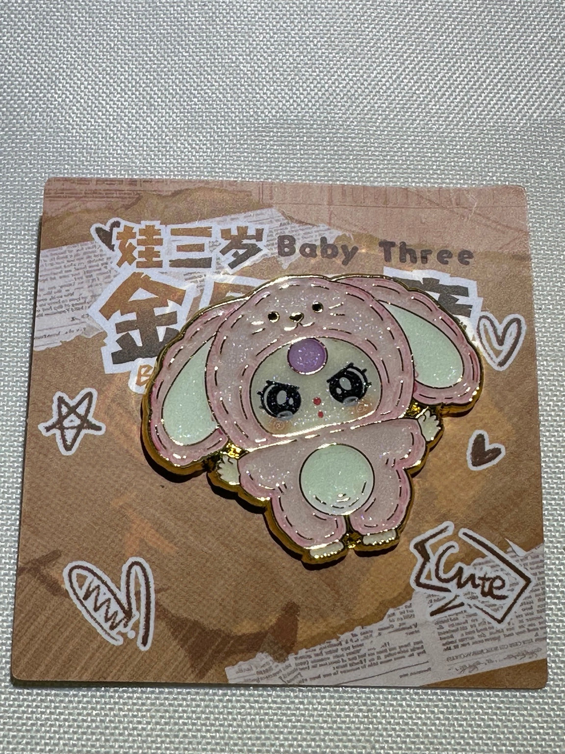 Baby Three Pink Bunny enamel pin with floppy ears, pale belly, and purple forehead accent on backing card