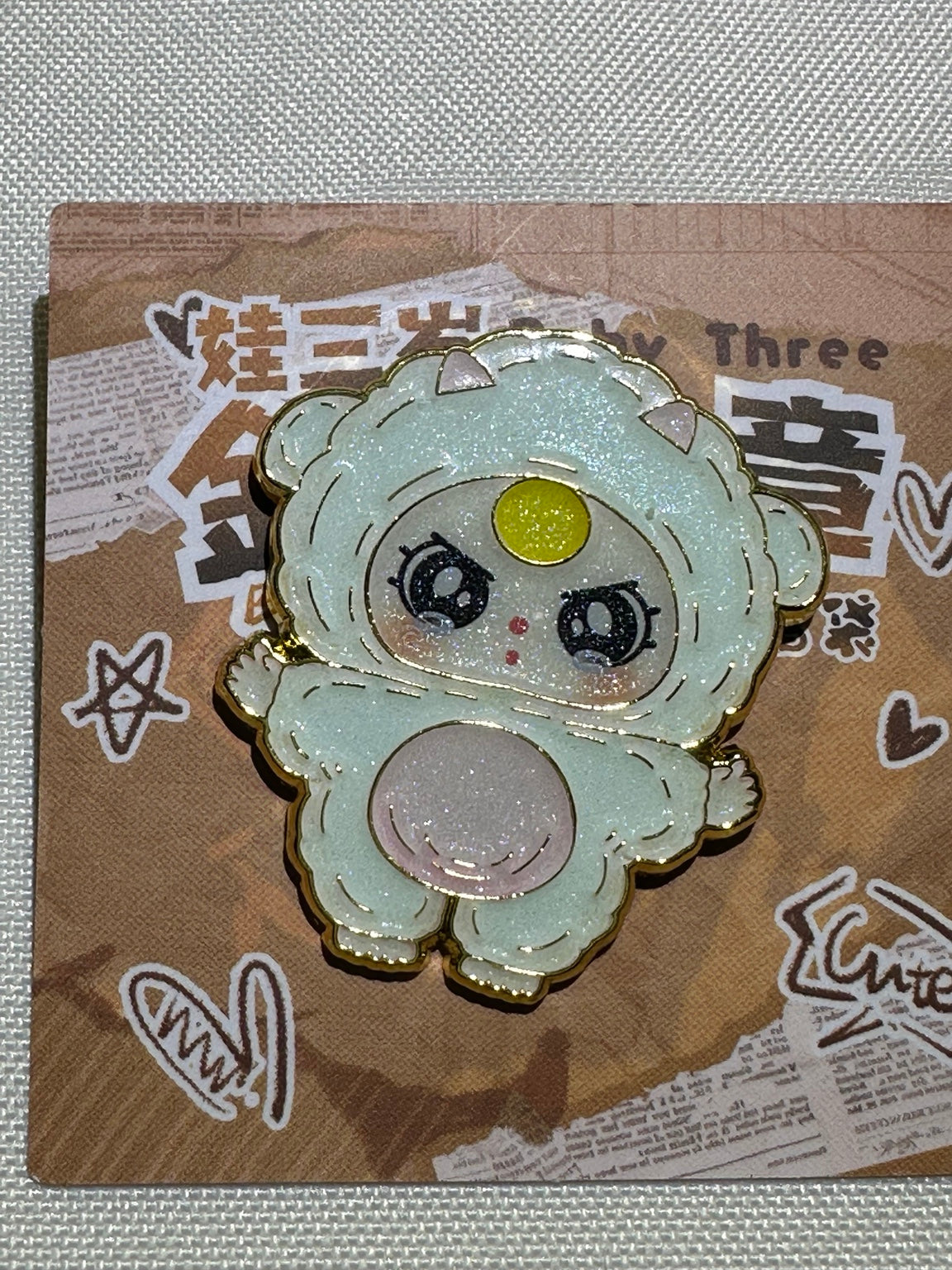 Baby Three Sheep enamel pin with pink belly, yellow forehead accent, and gold-colored outlines on backing card